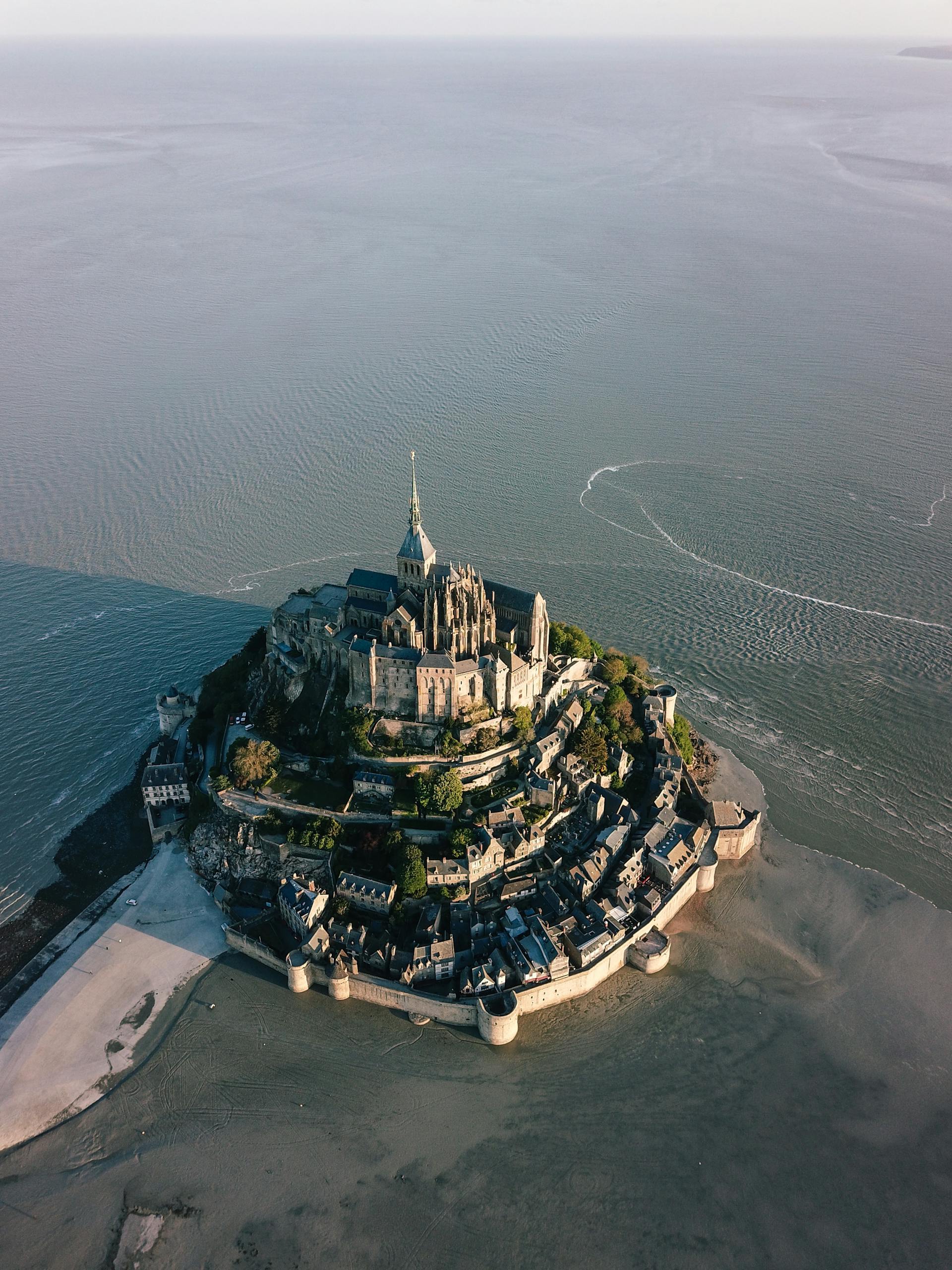 Stunning aerial view of Mont Saint Michel surrounded by the sea at low tide, showcasing its historic architecture.